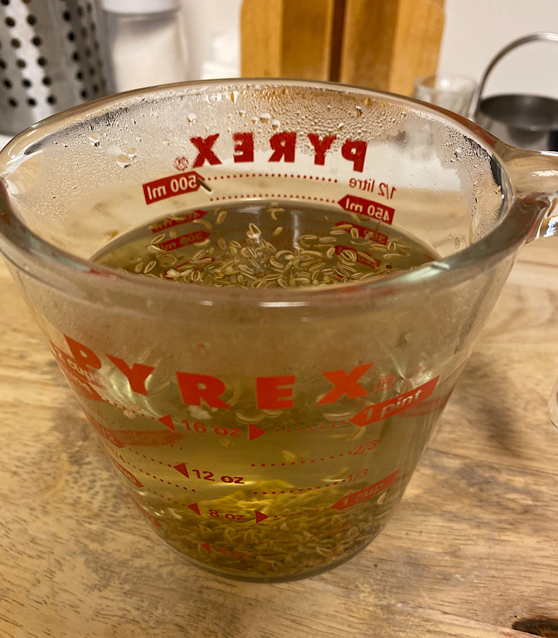 A measure glass cup with hot water with fennel seeds.