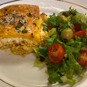 A plate with Chicken Vegetables Soufflé and green tomato, olives salad